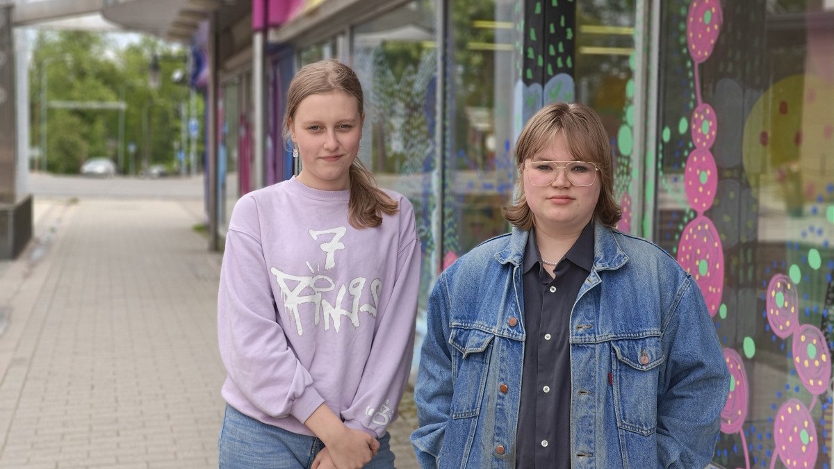 Kaksi nuorta seisovat Imatralla värikkään rakennuksen vierellä kävelykadulla.