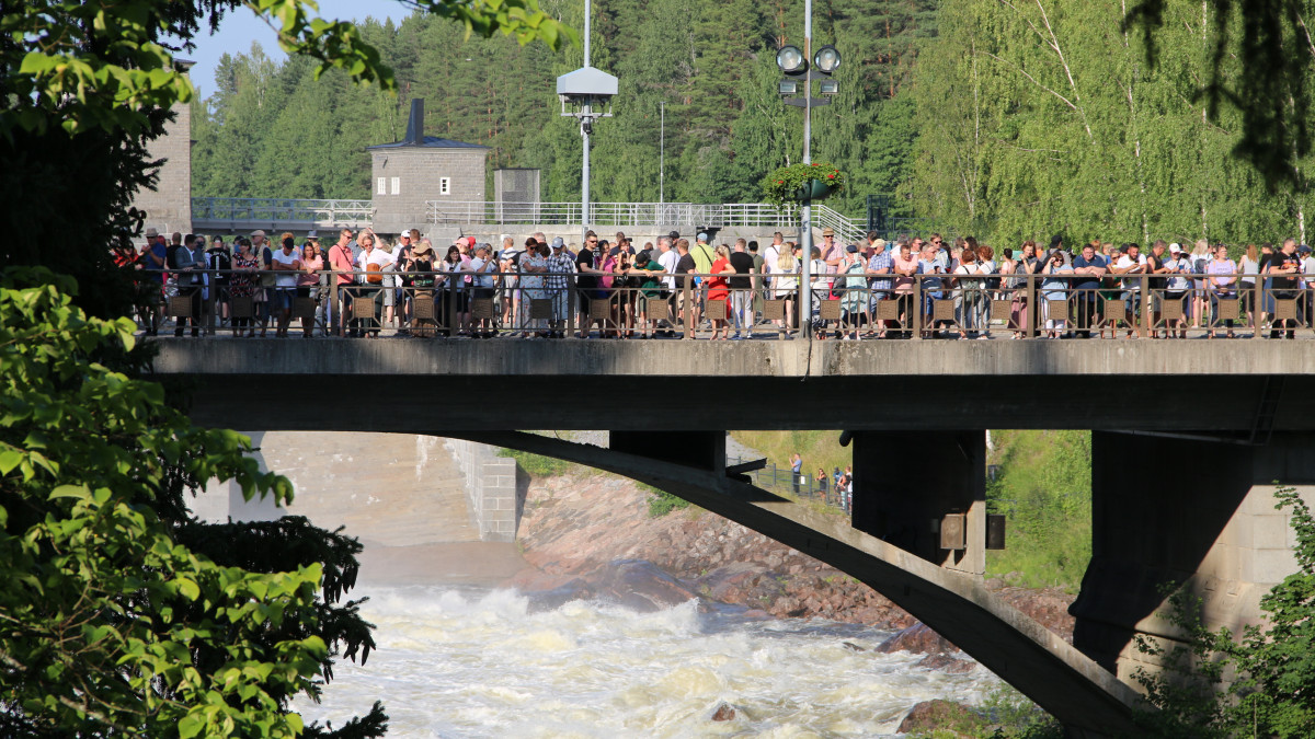 Yleisöä sillalla aurinkoisena kesäpäivänä katsomassa koskinäytöstä.