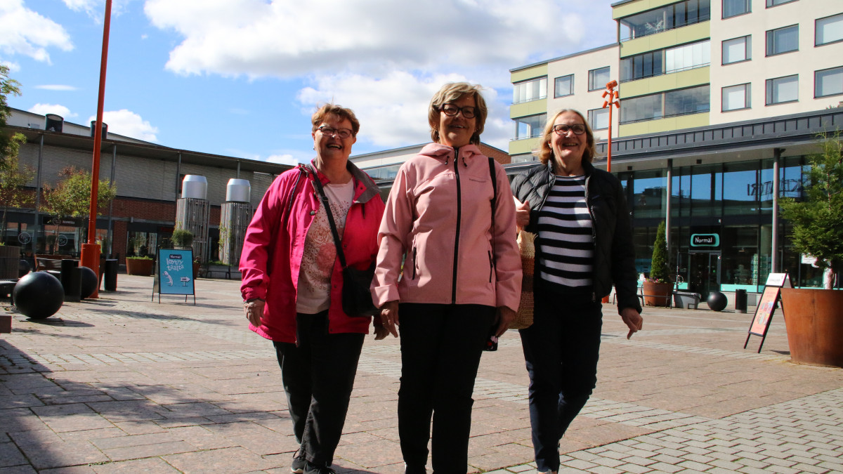 Kolme iäkästä naista kävelemässä aukiolla.