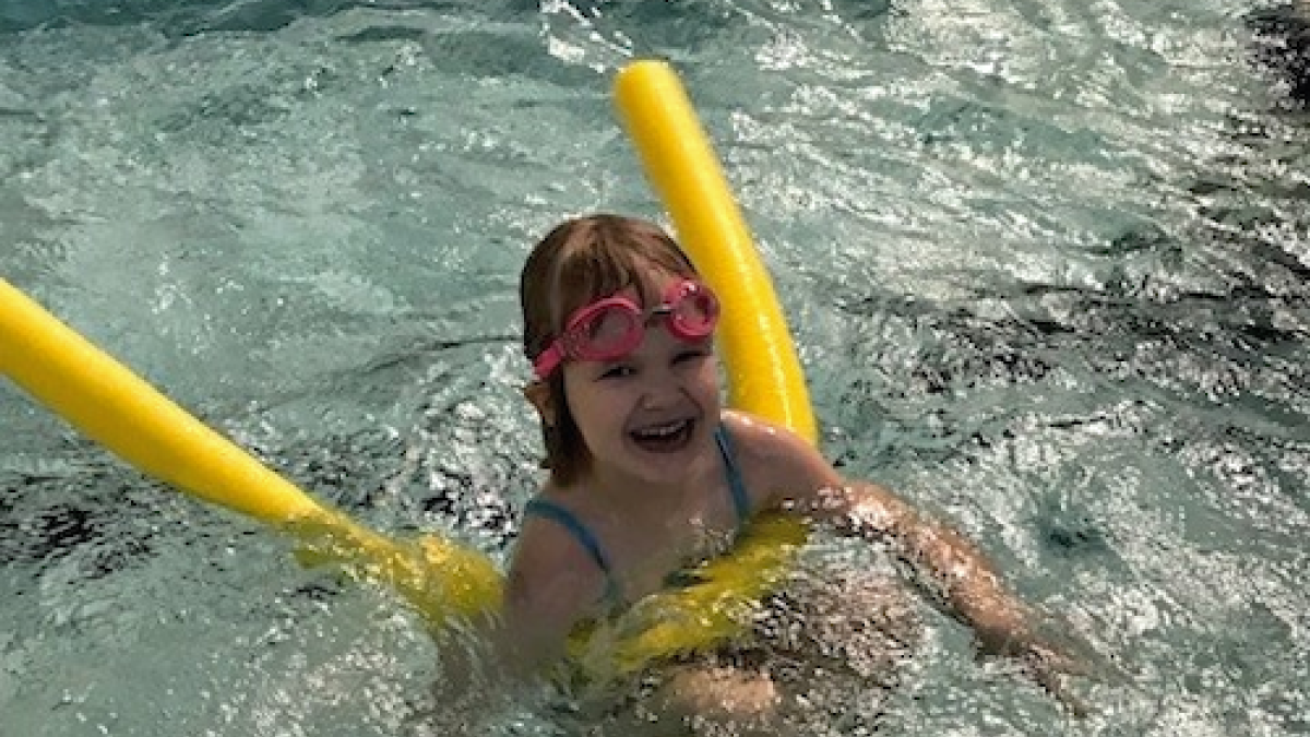 Lapsi uimassa altaassa keltaisen kellukkeen avulla hymy huulillaan.