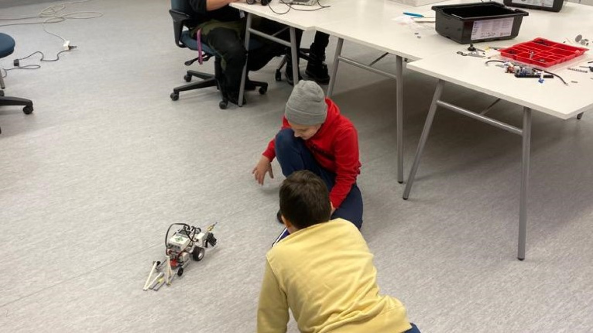Kaksi lastaa tutkii robottia lattialla.