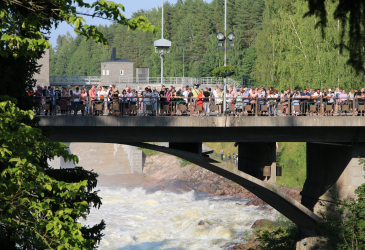 Yleisöä sillalla aurinkoisena kesäpäivänä katsomassa koskinäytöstä.
