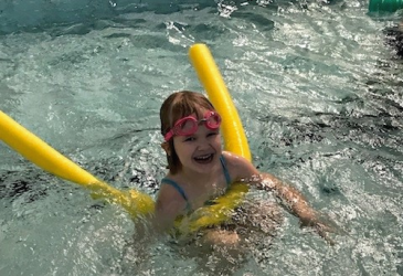 Lapsi uimassa altaassa keltaisen kellukkeen avulla hymy huulillaan.