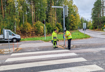 Kaksi huomiovaatteisiin pukeutunutta asentaa aurausviittoja risteyksessä.